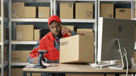 Young-Male-Postman-In-Uniform-Talking-On-Cellphone-And-Scanning-Parcel