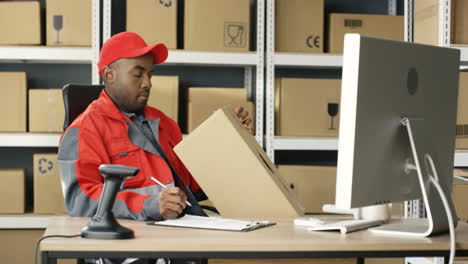 Postman-In-Uniform-Working-At-Computer-In-Post-Office-Store-With-Parcels