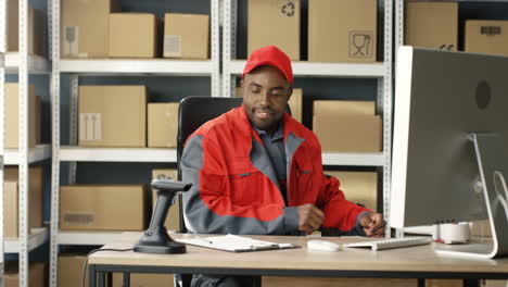 Young-Postman-In-Uniform-Working-At-Computer-In-Post-Office-Store