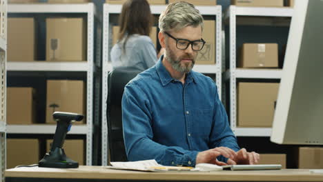 Gray-Haired-Man-In-Glasses-Working-At-Computer-Screen-In-Postal-Delivery-Store-And-Typing-On-Keyboard