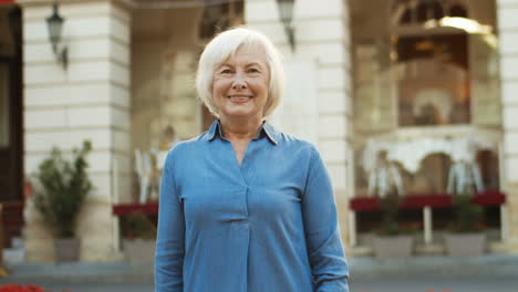 Portrait-Shot-Of-Beautiful-Gray-Haired-Old-Woman-In-Blue-Jeans-Shirt-Smiling-To-Camera-Outdoor