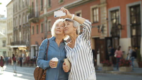 Dos-Hermosas-Ancianas-Sonriendo-Mientras-Toman-Una-Foto-Selfie-Con-Una-Cámara-De-Teléfono-Inteligente-En-La-Calle-En-El-Centro-De-La-Ciudad
