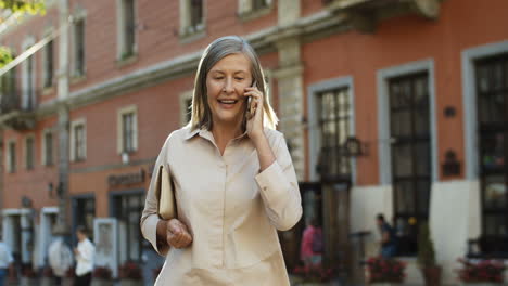 Senior-Good-Looking-Lady-Walking-The-Street-In-Old-City-And-Talking-On-Smartphone