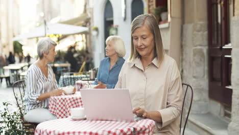 Good-Looking-Senior-Woman-With-Gray-Hair-On-Retirement-Typing-On-Laptop-Computer-At-Table-In-Cafe-Terrace-Outdoor
