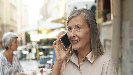 Close-Up-Of-Old-Woman-With-Grey-Hair-Talking-On-Mobile-Phone-While-Sitting-At-Cafe-Terrace