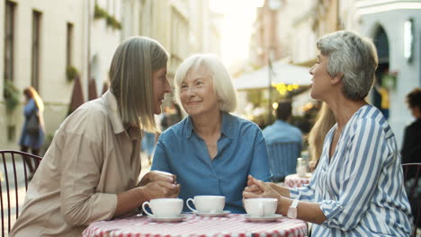 Beautiful-Happy-Women-Holding-Hands-And-Laughing-While-Sitting-At-Table-In-Cafe-Terrace