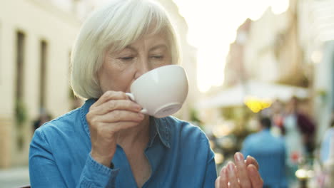 Nahaufnahme-Einer-Alten-Grauhaarigen-Rentnerin,-Die-Kaffee-Trinkt-Und-über-Etwas-Nachdenkt,-Während-Sie-Im-Café-Im-Freien-Sitzt