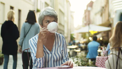 Beautiful-Senior-Woman-With-Short-Gray-Hair-Resting-At-Table-In-Cafe-Outside