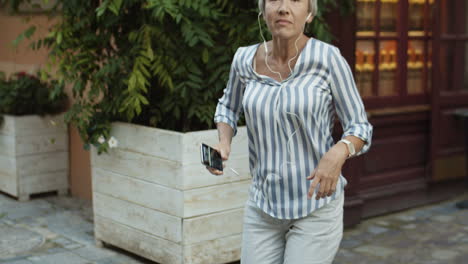 ältere-Glückliche-Und-Fröhliche-Frau,-Die-Musik-über-Kopfhörer-Auf-Dem-Smartphone-Hört-Und-Tanzt