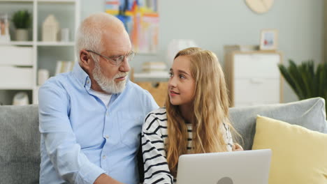 Close-Up-Of-The-Grey-Haired-Man-In-Glasses-Looking-On-The-Laptop-Screen-On-Which-His-Granddaughter-Playing-Or-Watching-Something