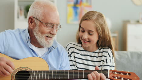 Nahaufnahme-Des-älteren-Grauhaarigen-Mannes-Mit-Brille,-Der-Für-Seine-Süße-Enkelin-Im-Wohnzimmer-Gitarre-Spielt