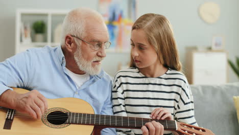 Porträtaufnahme-Des-Grauhaarigen-Großvaters,-Der-Gitarre-Spielt-Und-Seine-Enkelin-Unterrichtet