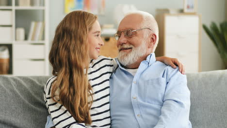 Portrait-Of-The-Cheerful-Grandfather-And-Granddaughter-Looking-At-Each-Other-And-Smiling,-Then-Looking-To-The-Camera