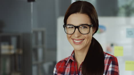 Portrait-Of-The-Young-Beautiful-Woman-In-Glasses-And-Red-Plaid-Shirt-Smiling-To-The-Camera-In-The-Office