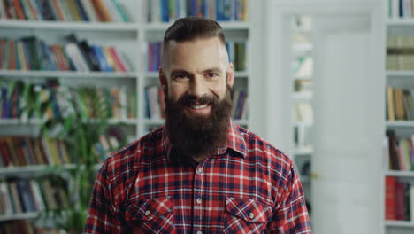 Portrait-Of-The-Hipster-Man-With-A-Beard-Looking-At-The-Side-And-Then-Smiling-Cheerfully-To-The-Camera-In-The-Library-Passage