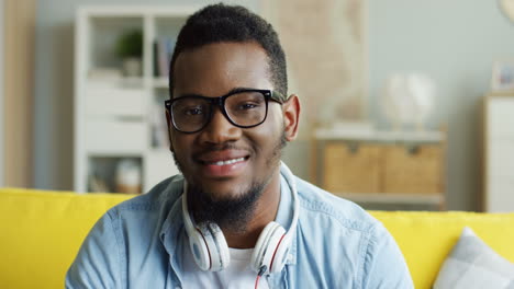 Portrait-Of-The-Young-Man-In-The-Glasses-And-With-A-Headphones-Smiling-To-The-Camera-While-Sitting-In-The-Living-Room