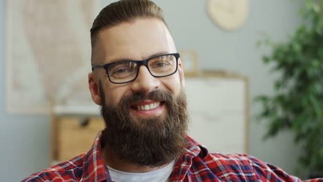 Portrait-Of-The-Serious-Young-Man-With-A-Beard-And-In-The-Glasses-Looking-Straight-To-The-Camera-And-Then-Smiling