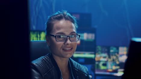 Portrait-Of-The-Young-And-Pretty-Woman-In-Glasses,-Software-Developer-Or-Hacker-Working-At-Night-At-The-Big-Screen-Of-Computer-In-The-Dark-Room-And-Then-Smiling-To-The-Camera-Happily