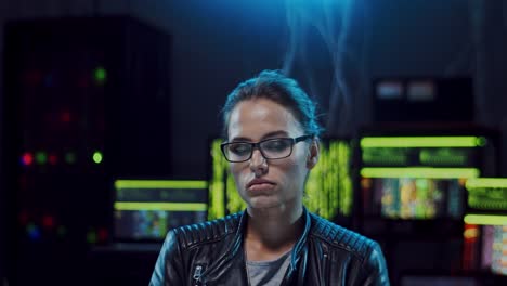 Portrait-Of-The-Young-Beautiful-Woman-Hacker-In-Glasses-Looking-Straight-To-The-Camera-While-Sitting-In-The-Dark-Server-Room-With-Computers