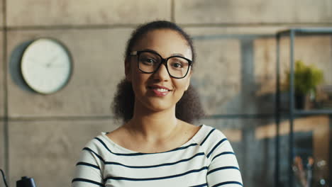 Portrait-Of-Mulatto-Joyful-Young-Woman-With-Eyeglasses-Posing-To-Camera-At-Workplace