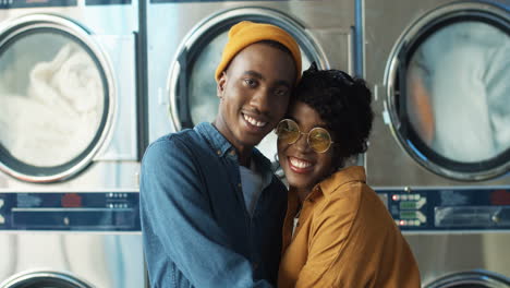 Portrait-Shot-Of-Happy-Attractive-Couple-In-Love-Hugging-And-Smiling-To-Camera-In-Laundry-Service