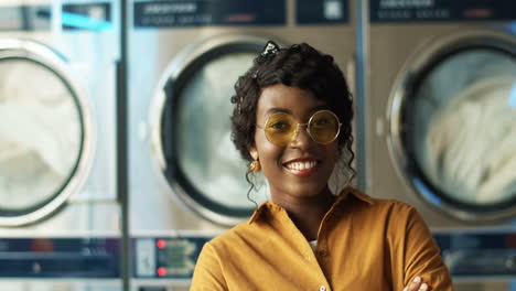 Close-Up-Of-Beautiful-Young-Woman-In-Yellow-Sunglasses-Smiling-Cheerfully-To-Camera-In-Laundry-Service-Room