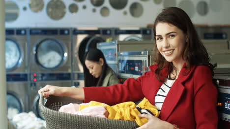 Portrait-Of-Beautiful-Stylish-Woman-Smiling-To-Camera-And-Holding-Basket-With-Dirty-Clothes-While-Standing-In-Laundry-Service