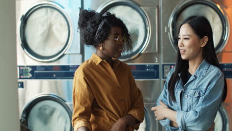 Mixed-Races-Stylish-Young-Girls-Best-Friends-Talking-And-Sharing-Secrets-While-Standing-In-Laundry-Service