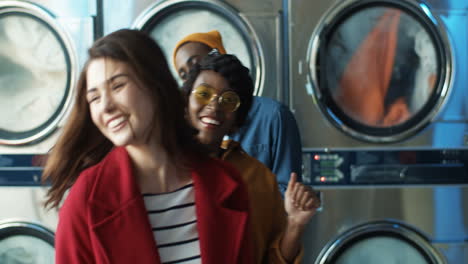 Young-Blurred-Multiethnic-Joyful-Stylish-Girls-And-Guy-Having-Fun-And-Dancing-In-Laundry-Service-Room-While-Machines-Washing-On-Background
