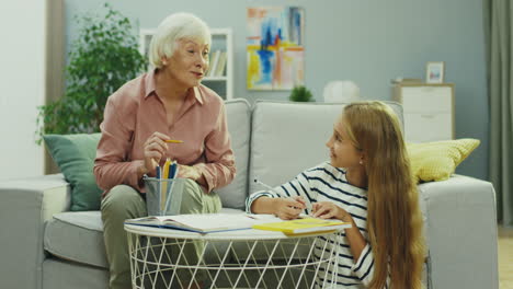 Grauhaarige-Seniorin,-Die-Zusammen-Mit-Ihrer-Jugendlichen-Enkelin-Schulhausaufgaben-Macht-Und-Ihr-Etwas-Erklärt