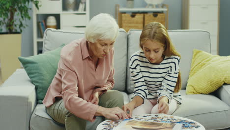 Großmutter-Und-Ihre-Hübsche-Teenager-Enkelin-Setzen-Puzzles-Zusammen,-Während-Sie-Zu-Hause-Auf-Dem-Sofa-Sitzen