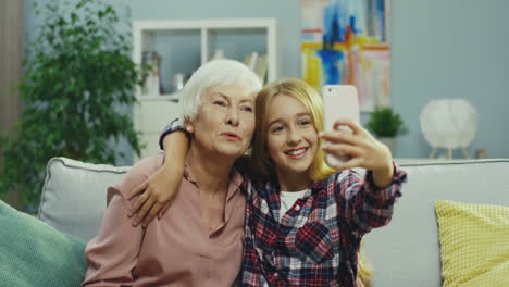 Nahaufnahme-Des-Süßen-Teenager-Mädchens-Und-Ihrer-Lächelnden-Grauhaarigen-Großmutter,-Die-Vor-Der-Smartphone-Kamera-Posieren,-Während-Sie-Zu-Hause-Ein-Selfie-Foto-Auf-Der-Couch-Machen