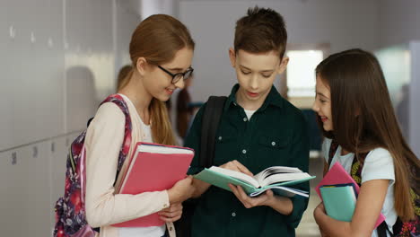 Cheerful-Cute-Children-Standing-At-The-School-During-The-Break-And-Looking-At-The-Textbook-With-Smiles,-Talking-About-Lessons