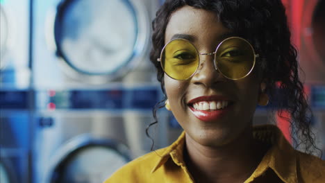 Close-Up-Of-Beautiful-Young-Woman-In-Yellow-Sunglasses-Smiling-Cheerfully-To-Camera-In-Laundry-Service-Room-1