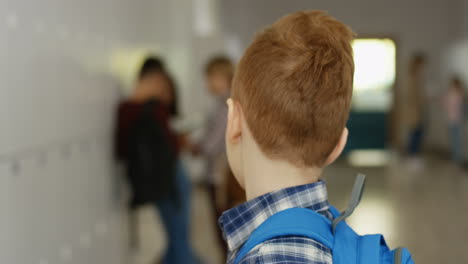 Portrait-Of-The-Little-Cute-Red-Haired-Schoolboy-With-Schoolbag-Turning-His-Head-To-The-Camera-And-Smiling-Straight-To-It-At-The-School-Corridor