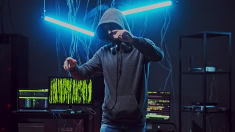 Young-Guy-Hacker-In-A-Hood-Listening-To-The-Music-And-Dancing-In-The-Dark-Neon-Room-With-Wires