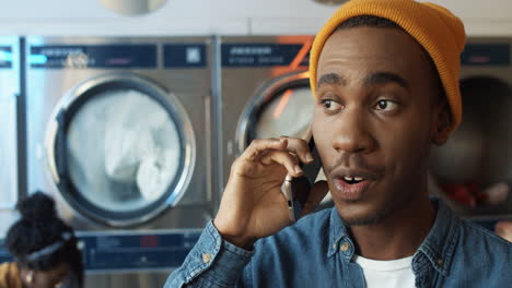 Close-Up-Of-Young-Cheerful-Handsome-Guy-In-Yellow-Hat-Talking-On-Mobile-Phone-And-Smiling-In-Laundry-Service-Room-Happy-Man-Speaking-On-Cellphone-In-Washhouse