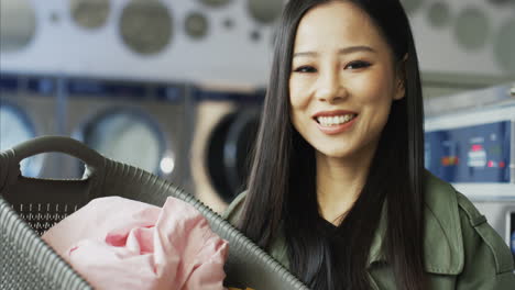 Portrait-Of-Pretty-Young-Woman-Holding-Basket-With-Clean-Clothes-After-Washing-And-Smiling-To-Camera
