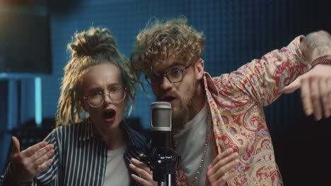 Portrait-Shot-Of-The-Stylish-Young-Man-And-Woman-In-Hipster-Style,-Singers-Of-The-Duo-Singing-In-The-Microphone-And-Recording-A-Song-In-The-Sound-Studio