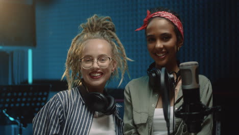 Portrait-Shot-Of-The-Young-Cheerful-Pretty-Girls,-Singer-Of-The-Duo,-Laughing,-Looking-At-Each-Other-And-Then-To-The-Camera-In-The-Sound-Studio-During-Recording