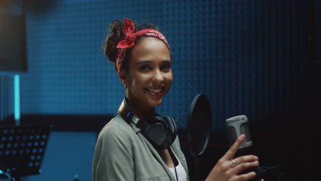 Portrait-Of-Young-Beautiful-Woman-Singer-Standing-At-The-Mic-In-The-Recording-Sound-Studio-And-Smiling-To-The-Camera-Happily