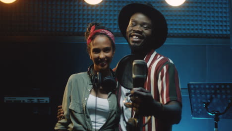 Portrait-Shot-Of-The-Mixed-Races-Stylish-Young-Man-And-Woman,-Singers-Of-The-Duo-Looking-At-Each-Other-And-Then-Smiling-To-The-Camera-In-The-Sound-Studio