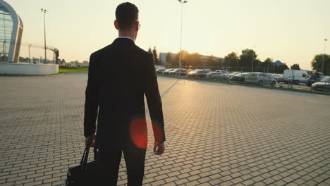Rear-On-The-Businessman-With-A-Bag-In-Hand-Going-Outside-To-The-Parking-On-The-Sunset-And-Camera-Moving-From-Feet-To-The-Head