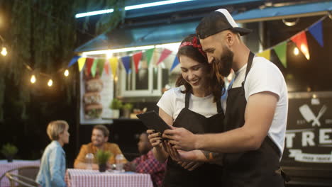 Cheerful-Young-Male-And-Female-Waiters-In-Aprons-Standing-Outdoors-At-Food-Truck-In-Park