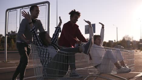 Side-View-Of-A-Young-Friends-Having-Fun-Outdoors-On-Shopping-Trolleys