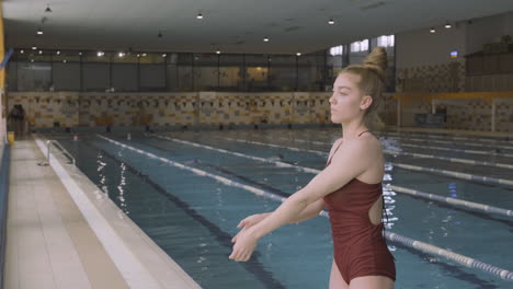 Beautiful-Young-Woman-Stretches-Arms-And-Shoulders-And-Concentrate-Before-Swimming-At-The-Indoor-Pool
