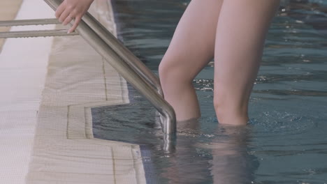 Close-Up-Of-A-Young-Woman's-Feet-Entering-The-Ladder-In-An-Indoor-Swimming-Pool