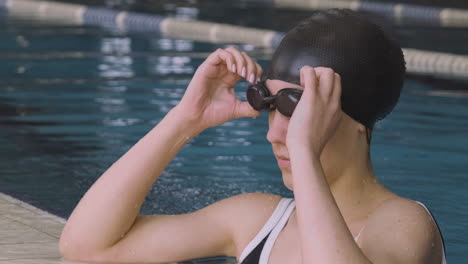 Close-Up-Of-A-Young-Woman-With-Swimming-Cap-And-Goggles-Diving-Into-The-Water-And-Resting-On-The-Edge-Of-The-Indoor-Pool