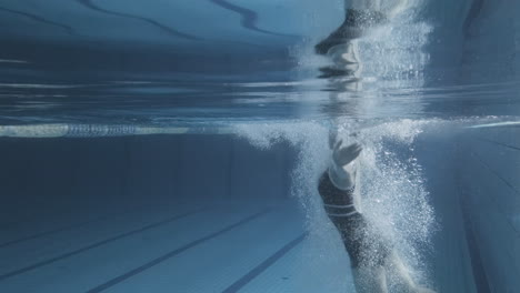 Unterwasseraufnahme-Einer-Jungen-Frau-Mit-Mütze-Und-Brille,-Die-In-Den-Pool-Springt