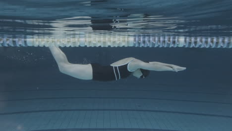 Unterwasser-Seitenaufnahme-Einer-Jungen-Schwimmerin-Mit-Badekappe-Und-Schutzbrille,-Die-In-Einem-Hallenbad-Taucht